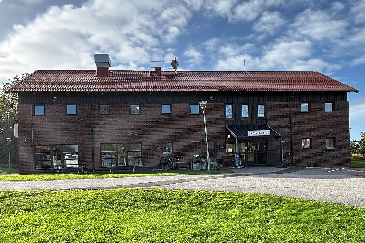 Rosenhills byggnad med grönt gräs i förgrunden och blå himmel ovanför