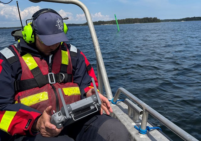 En man sitter i en båt och navigerar en drönare på havet