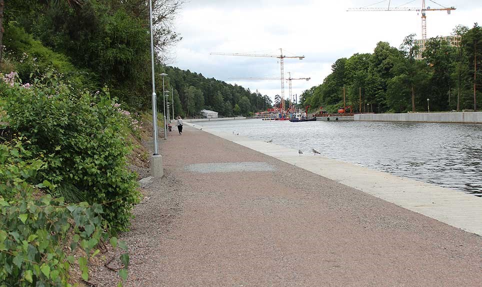 Bilden visar en promenadväg bredvid slussen i Södertälje. Byggkranar syns över kanalen