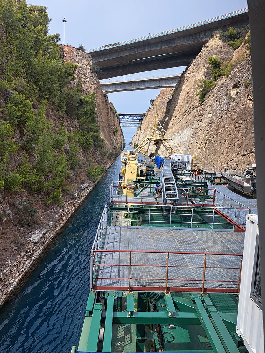 A ship is sailing through the Corinth Canal, which looks narrow