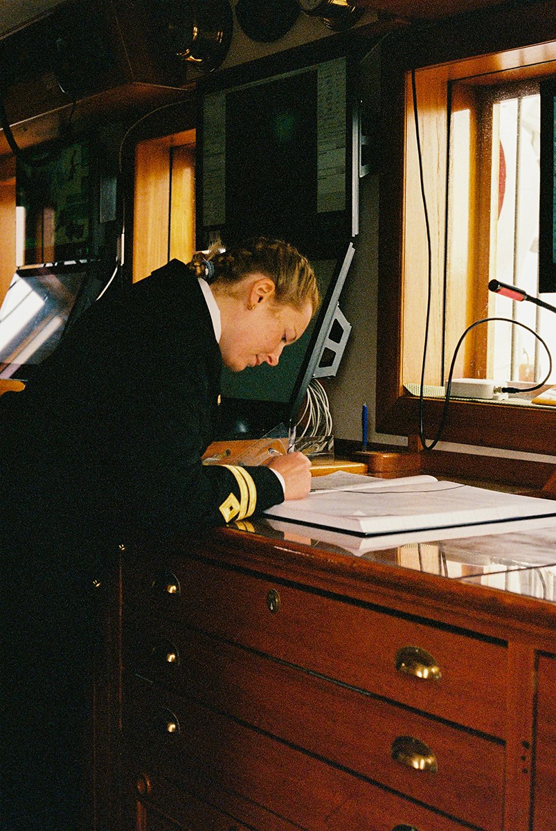A woman in uniform writes in the logbook, which is placed on an old wooden sideboard on a old ship