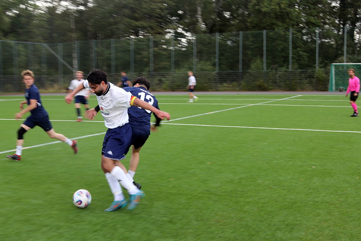 En spelare i vit dress har kontroll över bollen efter en drabbning mot en i blå dress