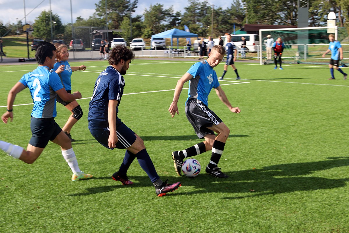 Fyra spelare i närbild. Solen kastar skuggor på konstgräset, när de jagar bollen