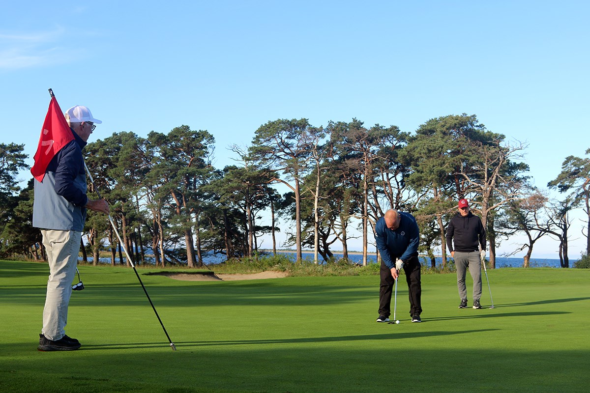 Tre golfspelare på green. En puttar en håller i flaggan.