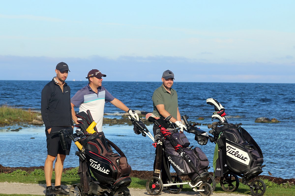 Tre golfspelare med deras bagar. Öppet vatten i bakgrunden
