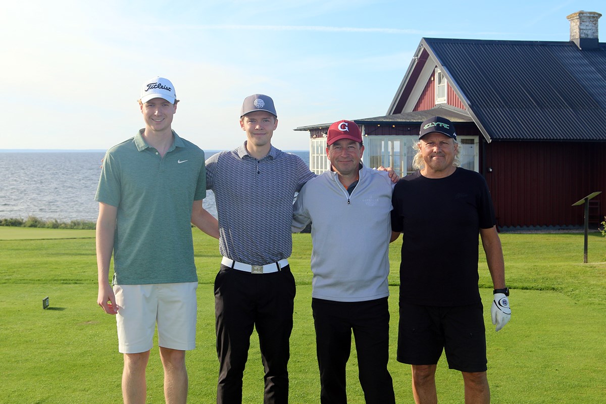 Fyra muntra spelare uppställda framför en röd stuga vid vattnet