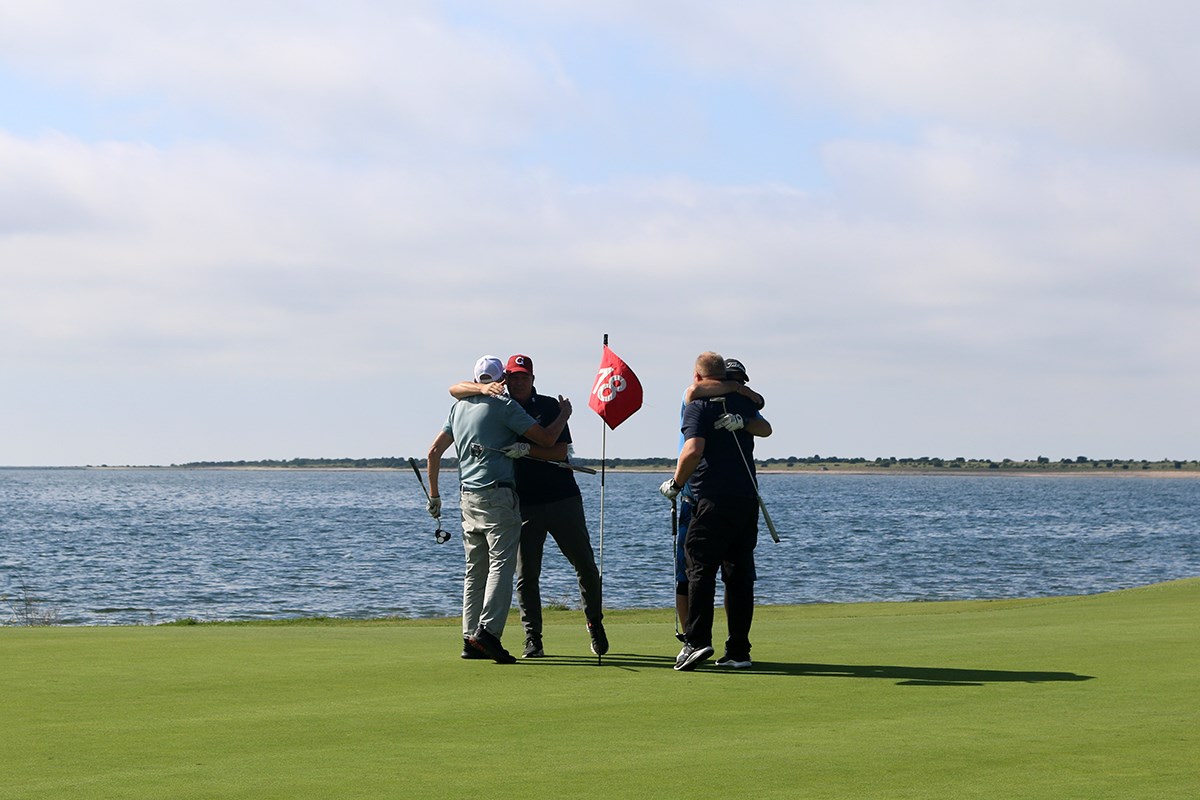 Fyra golfare kramar om varandra vid hålets flagga