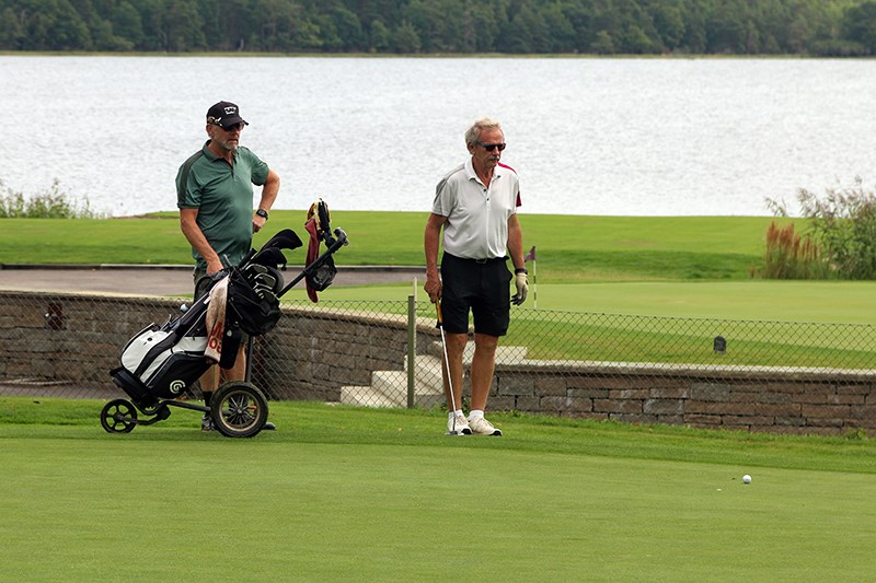Två golfare står på golfbanan och blickar bortåt. Vatten i bakgrunden