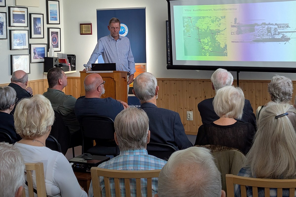 En skara människor sitter och lyssnar till en föredragshållare, som visar en presentation